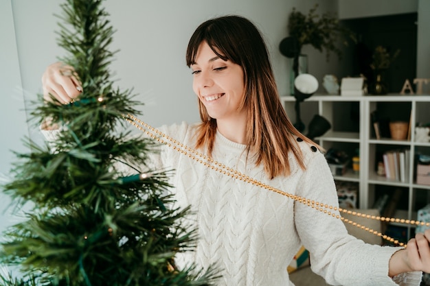 Foto mujer joven feliz preparando su casa para navidad. decoración de árbol con bonitas bolas navideñas.