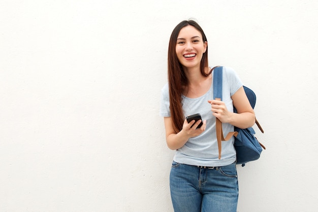 Mujer joven feliz que se coloca con la mochila y el teléfono móvil