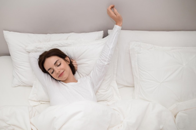 Mujer joven feliz que se extiende en la cama después de despertarse