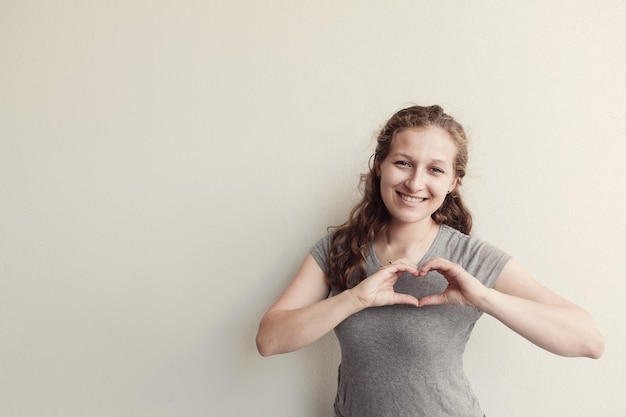 Mujer joven feliz que hace sus manos en forma del corazón