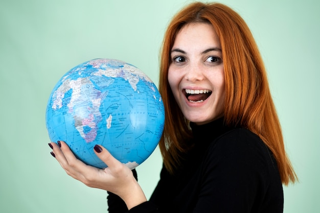 Mujer joven feliz que sostiene un globo geográfico en sus manos.