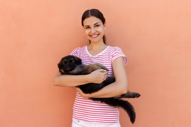 Mujer joven feliz que sostiene su perrito del animal doméstico en fondo anaranjado