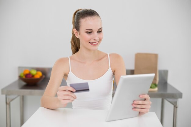 Mujer joven feliz que usa su tableta para ir de compras en línea