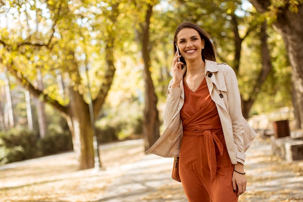 Mujer joven feliz que usa el teléfono celular en parque del otoño