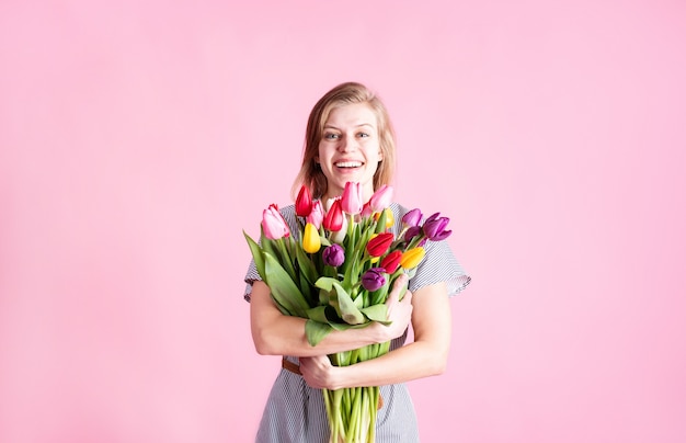 Mujer joven feliz con ramo de tulipanes frescos aislado sobre fondo rosa