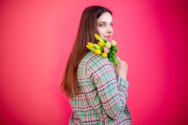 Mujer joven feliz con ramo de tulipanes sobre fondo rosa