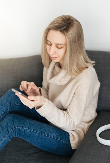 Mujer joven feliz relajándose en un cómodo sofá sosteniendo un teléfono inteligente en las manos