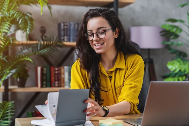 Mujer joven feliz revisando su bloc de notas mientras trabaja desde el escritorio