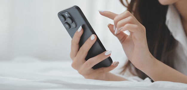 Mujer joven feliz con ropa casual sonriendo y mirando a la cámara mientras usa la computadora portátil en la cama en el dormitorio en casa