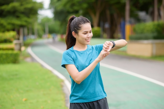 Una mujer joven feliz en ropa deportiva con reloj inteligente mientras hace ejercicio en el parque