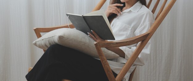 Mujer joven feliz con ropa informal sonriendo y mirando a la cámara mientras usa una computadora portátil en la cama en el dormitorio en casa