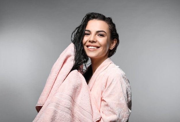 Mujer joven feliz secando el cabello con una toalla después de lavarlo en un fondo gris claro