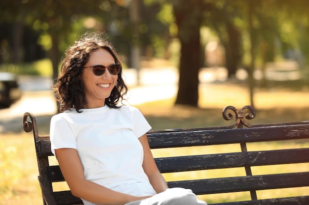 Mujer joven feliz sentada en un banco en el parque