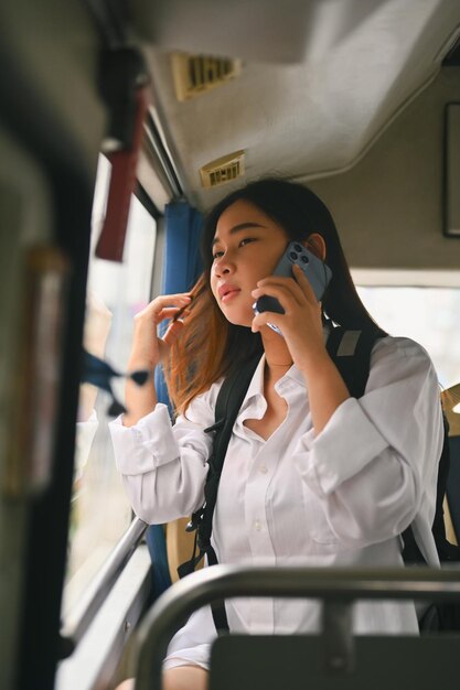 Mujer joven feliz sentada dentro del transporte público en autobús y hablando por teléfono móvil