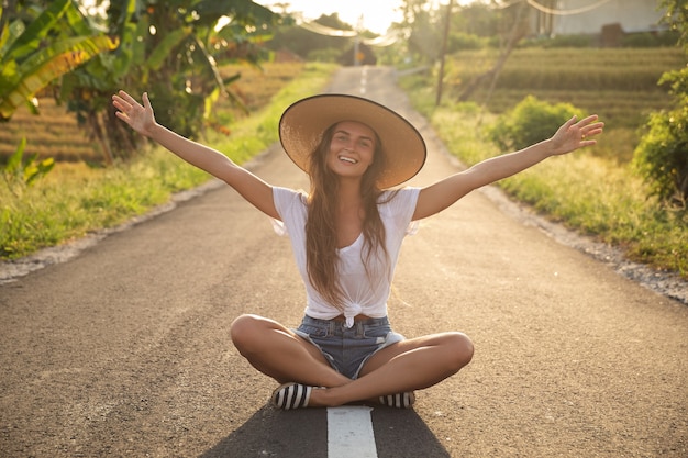 Foto mujer joven feliz está sentada en medio de la carretera asfaltada