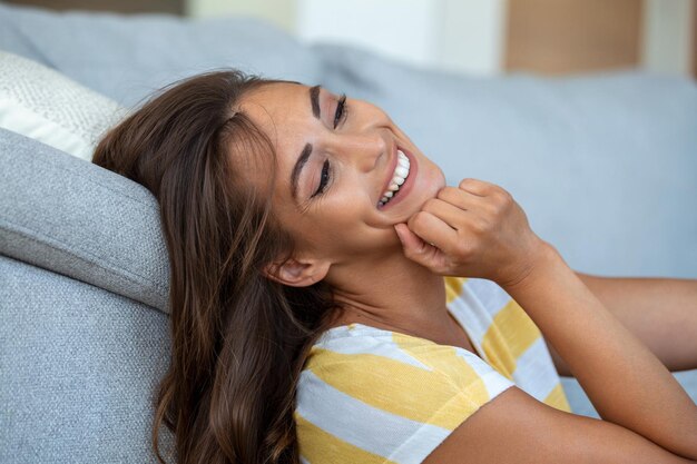 Mujer joven feliz sentada en el sofá en casa Retrato de mujer hermosa sonriendo y relajándose durante el verano