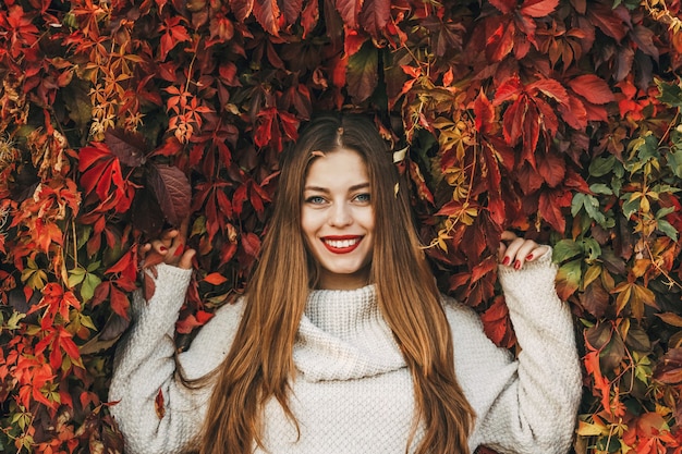 Mujer joven feliz sobre una pared de hojas de hiedra roja.