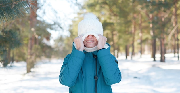 Mujer joven feliz con sombrero blanco de punto en el bosque nevado de invierno divirtiéndose