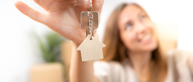 Mujer joven feliz sonriendo con el nuevo llavero de llaves de casa con pancarta de bienes raíces de casa de madera