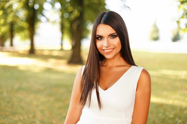 Foto mujer joven feliz con una sonrisa en un vestido blanco en un día de verano cerca de árboles