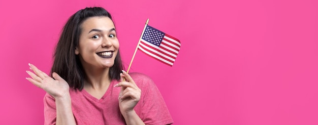 Mujer joven feliz sosteniendo la bandera estadounidense contra un fondo rosa de estudio