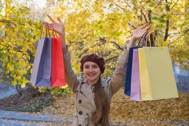 Mujer joven feliz sosteniendo bolsas de compras en el fondo del parque de otoño Venta Otoño