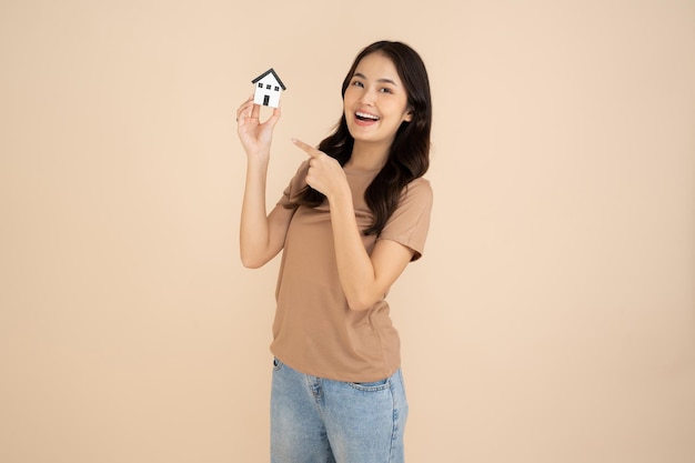 Mujer joven feliz sosteniendo un modelo de casa de pie en el estudio