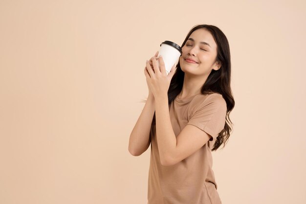 Mujer joven feliz sosteniendo una taza de café de pie en el estudio