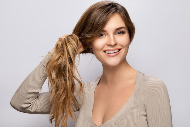 Foto mujer joven está feliz con su cabello hermoso y saludable sobre fondo gris