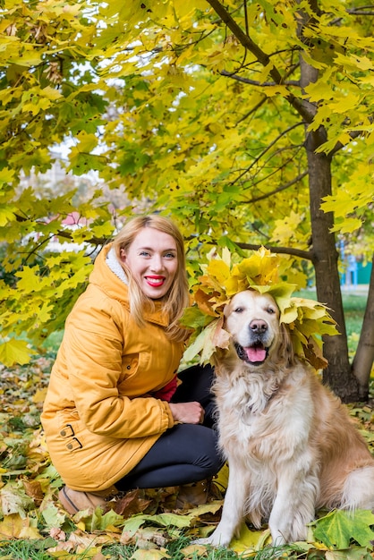 Mujer joven feliz con su perro perdiguero entre hojas amarillas de otoño.