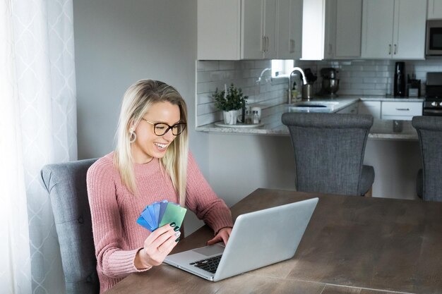 Foto mujer joven feliz con tarjetas de crédito mientras usa una computadora portátil en casa