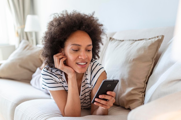 Mujer joven feliz con teléfono móvil tendido en el sofá