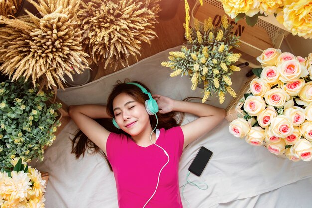 Mujer joven feliz tendida en el suelo a escuchar música a través de un teléfono inteligente, vista superior