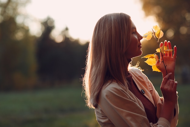 Mujer joven feliz tiene hojas de otoño en la mano en el parque de otoño.