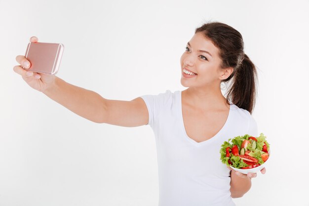 Mujer joven feliz tomar un selfie con ensalada de verduras