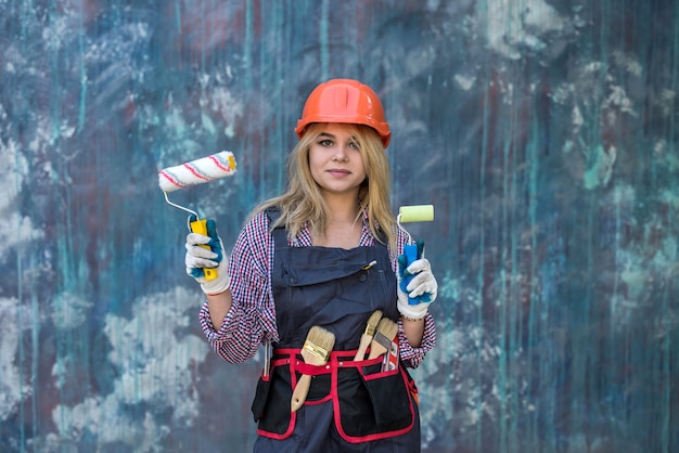 Mujer joven feliz en uniforme que sostiene el rodillo de pintura cerca de la pared de color. Concepto de decoración del hogar