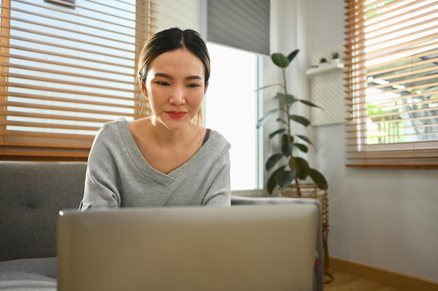 Mujer joven feliz usando una computadora portátil en casa chateando con amigos en las redes sociales viendo películas y comprando en línea