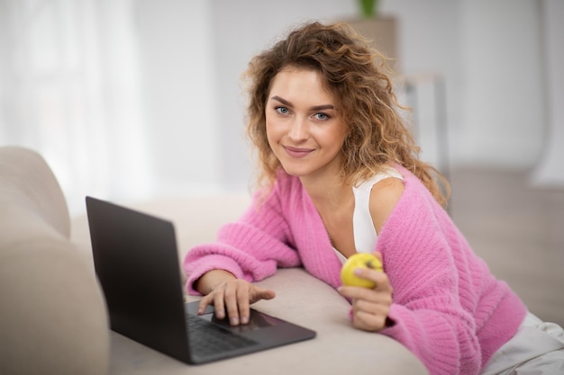 Mujer joven feliz usando laptop y comiendo manzana en casa