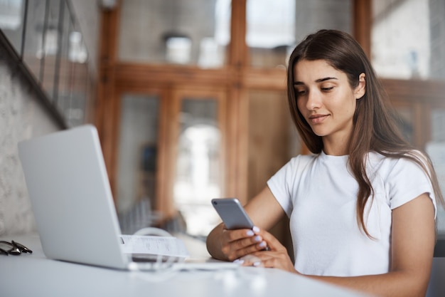 Mujer joven feliz usando un teléfono celular inteligente para mirar sus selfies y elegir una nueva imagen de perfil en las redes sociales.