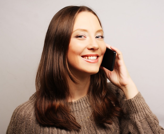 Mujer joven feliz usando un teléfono móvil aislado sobre un fondo blanco.