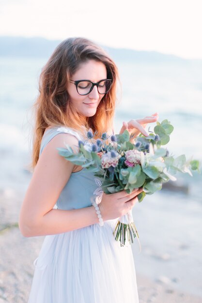 Mujer joven feliz en vestido elegante con el ramo de flores y sonriendo cerca del lago de Garda. Italia