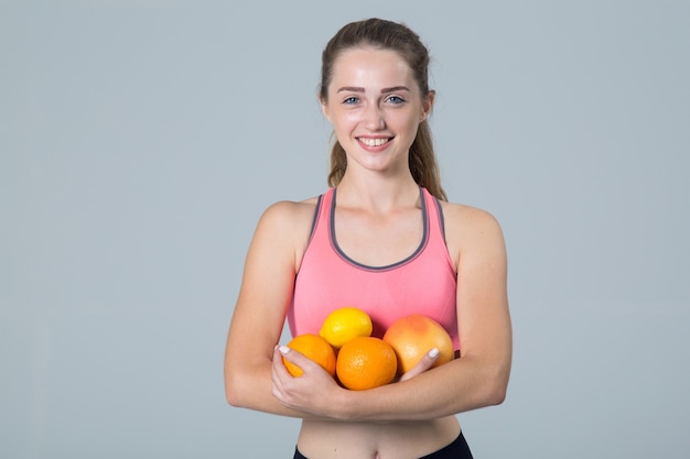 Mujer joven fitness con cítricos en sus manos en gris claro