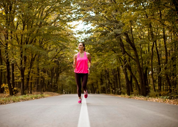 Mujer joven fitness corriendo en la pista forestal en otoño dorado