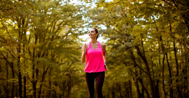 Mujer joven fitness corriendo en la pista forestal en otoño dorado