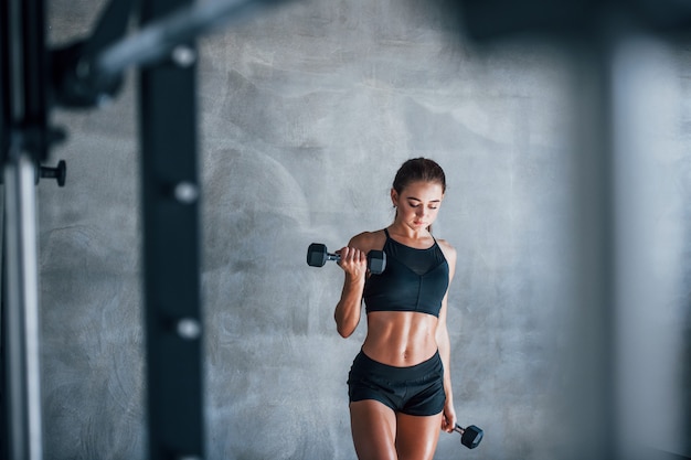 Mujer joven fitness está en el gimnasio con pesas en las manos.