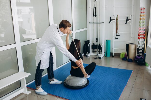 Mujer joven fitness haciendo ejercicio de rehabilitación de kinesioterapia con especialista en rehabilitación personal en el gimnasio