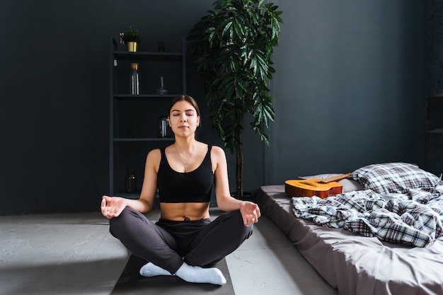 Mujer joven fitness meditar, hacer yoga en el interior en casa cerca de la cama