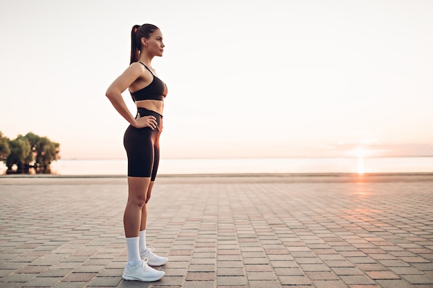 Mujer joven fitness de pie en la playa al amanecer.