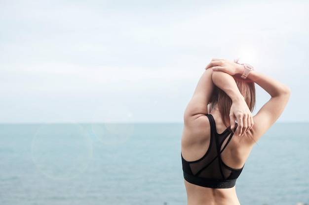 Mujer joven fitness en ropa deportiva estirando el cuerpo contra la vista al mar, ejercicio de mujer saludable en la mañana. Conceptos de equilibrio de vida laboral, bienestar y entrenamiento