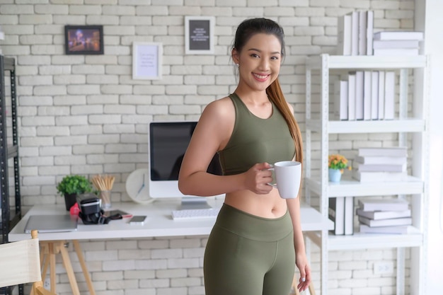 Mujer joven fitness en ropa deportiva tomando una taza de café después de hacer ejercicio en casa